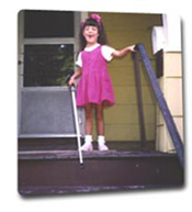 Young child with cane stands at top of stairs